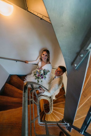 Braut und Bräutigam stehen auf einer Treppe, umgeben von Holz und Licht.